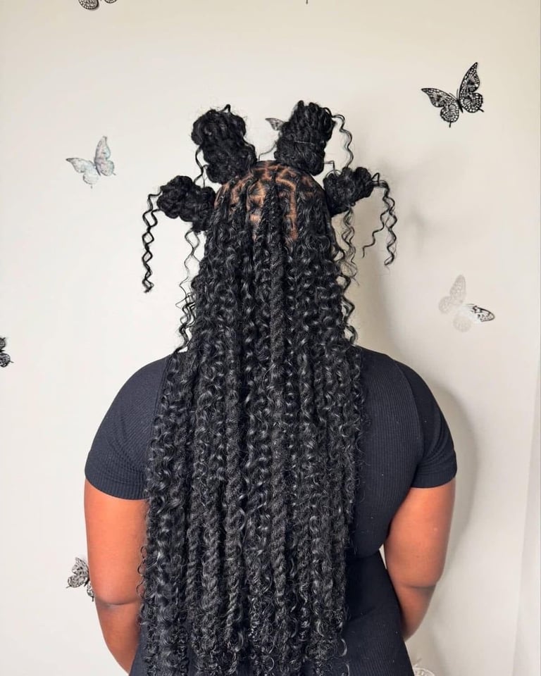 Back view of person with long black braids styled with four buns and curled ends, wearing navy and orange shirt against wall with butterfly decorations