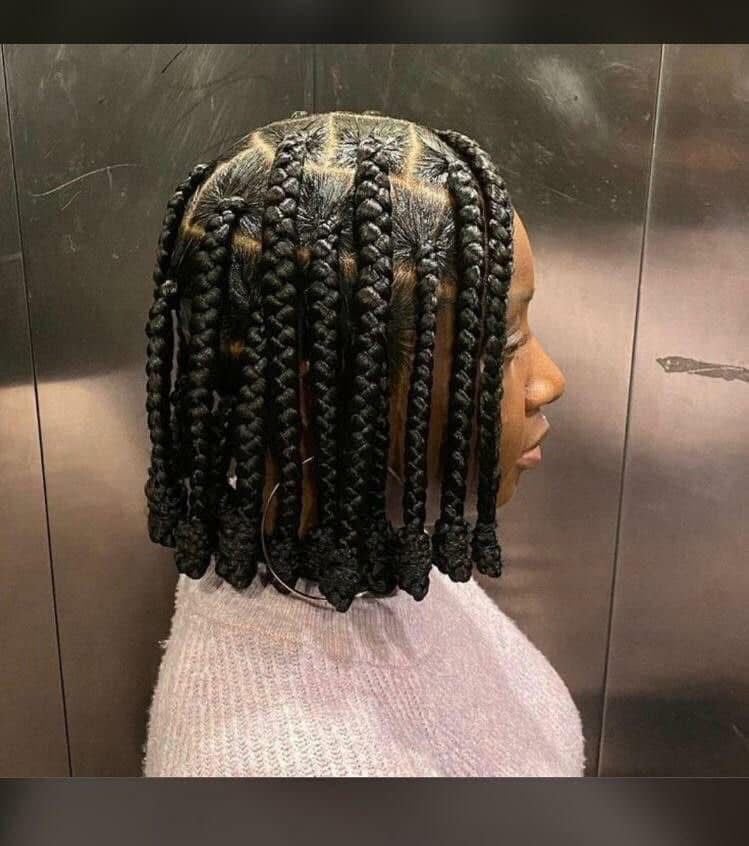 Profile view of a person wearing shoulder-length box braids with a light-colored sweater against a metallic background
